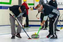 Two curlers sweeping a yellow stone
